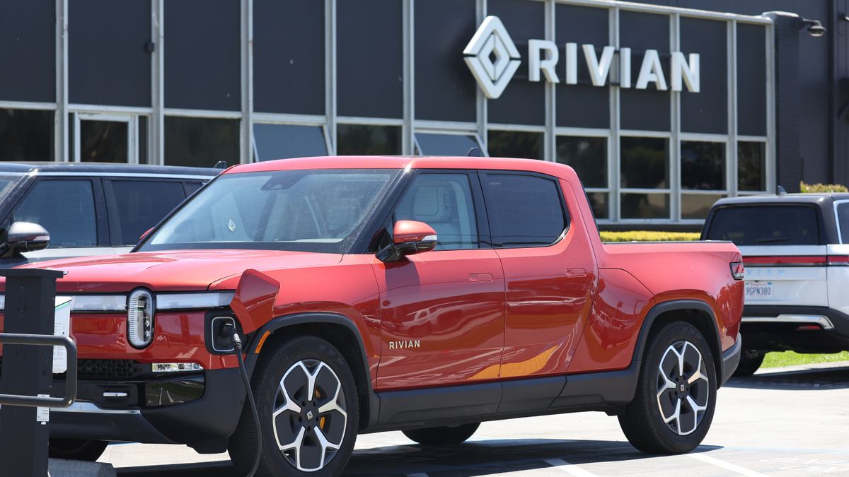 A red Rivian R1T pickup parked in front of a Rivian service center.