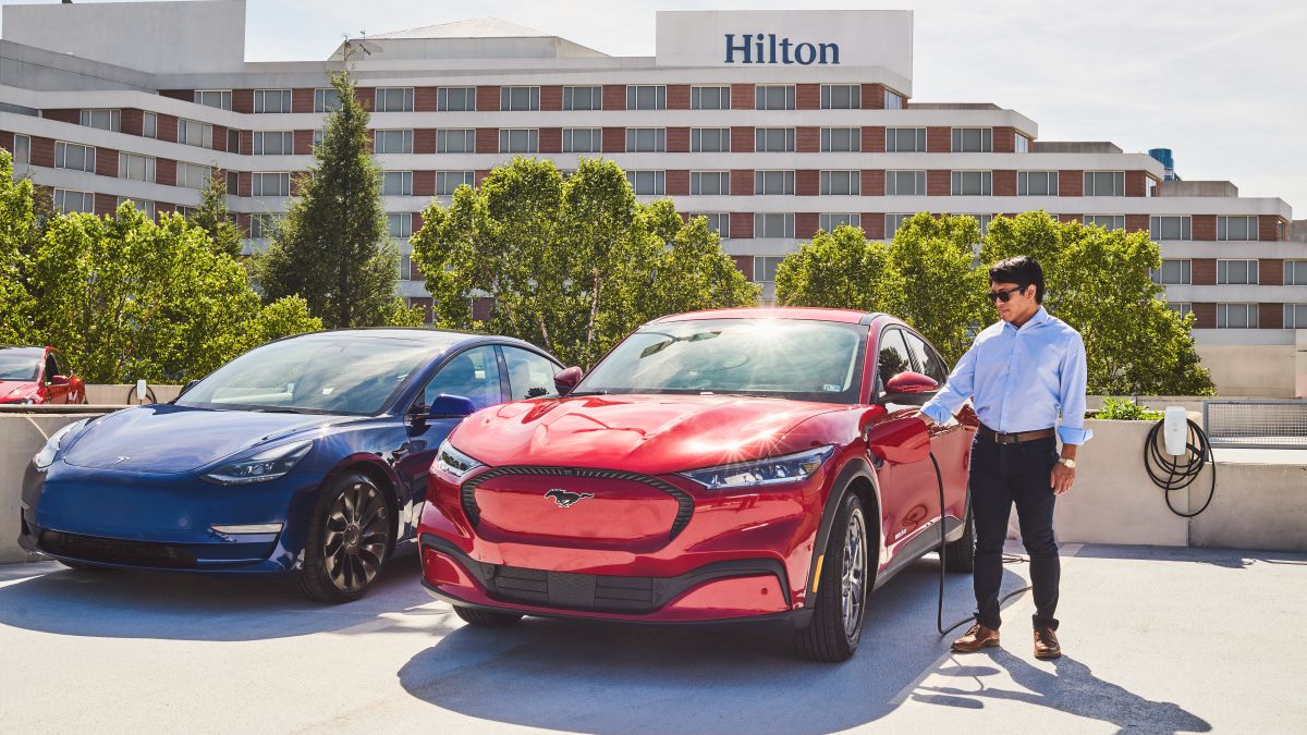 An image of two Tesla cars in front of a Hilton hotel being charged via an EV charging station.